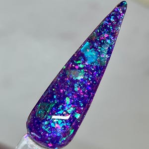 May include: A close-up of a purple nail polish with iridescent glitter. The glitter is a mix of blue, green, and pink.