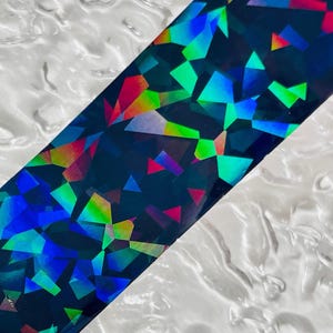 May include: A holographic sticker with a geometric pattern in shades of blue, green, red, and purple on a black background.