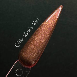May include: A nail polish swatch in a deep brown shade with shimmering gold and pink flecks. The text "C812- Worm's Wart" is written in white script along the side of the swatch. The swatch is on a clear plastic stick.