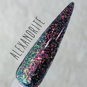 May include: A close-up of a black nail polish with iridescent green, pink, and gold glitter. The text "ALEXANDRITE" is written on the nail polish bottle.