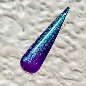 May include: A close-up of a purple and teal nail polish with a shimmery finish.