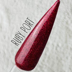 Puede incluir: Primer plano de un esmalte de uñas rojo oscuro con acabado brillante. El esmalte está etiquetado como "RUBY PORT".