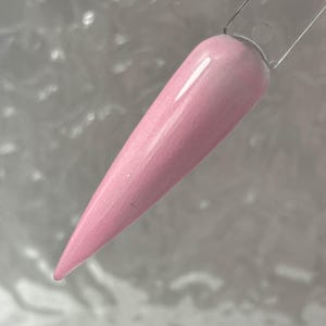 May include: A close-up of a pink nail polish with a shimmery finish. The polish is applied to a nail tip.