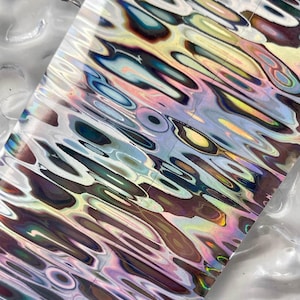 Op de afbeelding: Een vel iriserende holografische vinyl met een golvend, abstract patroon in tinten blauw, groen, paars en bruin.