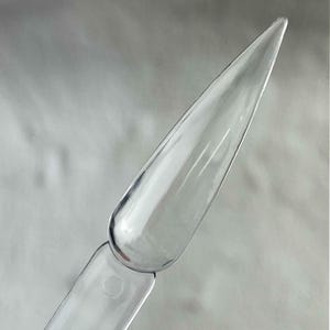 Puede incluir: Un palito de muestra de uñas transparente y claro con una punta. La herramienta de arte de uñas está hecha de plástico transparente y está diseñada para mostrar colores de esmalte de uñas o diseños de arte de uñas. El palito de muestra es utilizado por técnicos de uñas y entusiastas del arte de uñas.