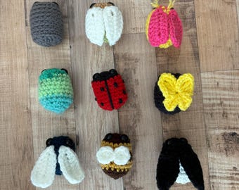 May include: A collection of ten crocheted insect toys. The toys are in various colors, including black, white, red, yellow, green, and blue. The toys are all about 2 inches tall and are made with a variety of stitches.
