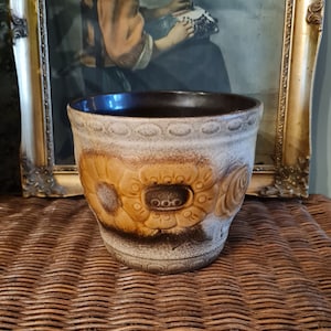 May include: A brown and white ceramic planter with a floral design. The planter has a wide rim and a rounded base.