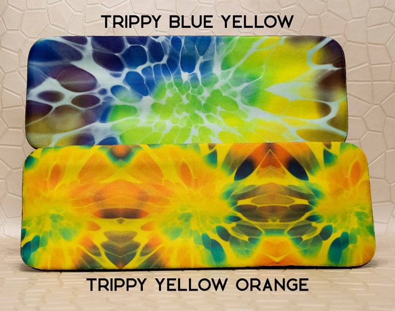 Op de afbeelding: Twee rechthoekige brillenkokers met kleurrijke tie-dye patronen. De bovenste koker heeft een blauw, geel en groen ontwerp, met de tekst "Trippy Blue Yellow". De onderste koker heeft een geel en oranje ontwerp, met de tekst "Trippy Yellow Orange".