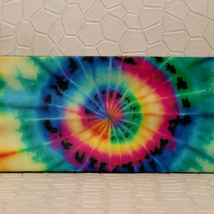 Op de afbeelding: Rechthoekige brillenkoker met een levendig tie-dye patroon. Het ontwerp toont een spiraal van kleuren, waaronder roze, geel, groen en blauw. De koker heeft afgeronde hoeken en een zwarte rand.