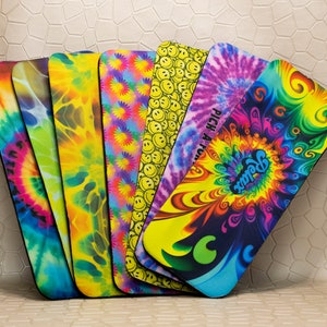 Op de afbeelding: Een verzameling kleurrijke yogamatten met diverse patronen. De ontwerpen omvatten tie-dye, smiley gezichten en psychedelische swirls. E&eacute;n mat heeft het woord "Relax". De matten worden getoond tegen een neutrale achtergrond. Elke mat is ongeveer 60 cm lang.