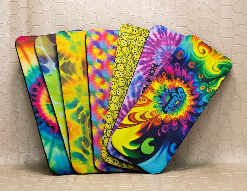 Op de afbeelding: Een verzameling kleurrijke yogamatten met diverse patronen. De ontwerpen omvatten tie-dye, smiley gezichten en psychedelische swirls. E&eacute;n mat heeft het woord "Relax". De matten worden getoond tegen een neutrale achtergrond. Elke mat is ongeveer 60 cm lang.