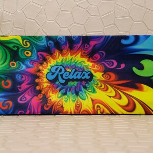 Op de afbeelding: Een rechthoekige etui met een levendig, psychedelisch ontwerp. De etui heeft een wervelend patroon van kleuren, waaronder geel, groen, blauw, roze en paars. Het woord "Relax" staat in een blauw, retro lettertype in het midden.