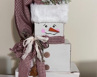 Puede incluir: Decoración de muñeco de nieve artesanal hecha de bloques de madera blancos apilados. Presenta un sombrero, bufanda y lazo a cuadros burdeos y blancos. El muñeco de nieve tiene una cara pintada, botones y adornos.