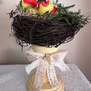 Entzückende Vögel in einem Nest mit gesprenkelten Eiern und darauf sitzt ein oben bemalter und gealterter Kerzenständer. Niedliche sommerliche Vogel Dekoration.