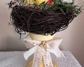 Adorabili uccellini in un nido con uova maculate, appollaiati su un candelabro giallo dipinto e anticato. Graziosa decorazione estiva a forma di uccellino.