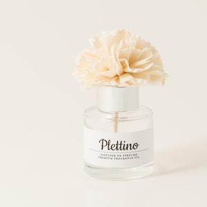 May include: A clear glass perfume diffuser bottle with a white label that reads "Plettino". The bottle is topped with a silver cap and a cream-colored, flower-shaped diffuser. The product is a premium fragrance oil.