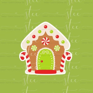 May include: A gingerbread house cookie cutter with white icing, red candy dots, green and white candy swirls, and red and white candy canes. The cookie cutter is on a green background.
