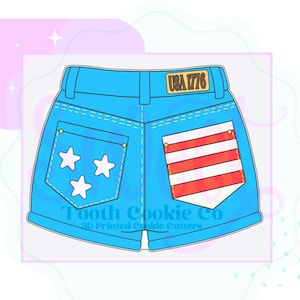May include: A blue cookie cutter shaped like denim shorts. The shorts have two back pockets, one with three white stars and the other with red and white stripes. The text "USA 1776" is on a yellow patch. The text "Tooth Cookie Co" is at the bottom.