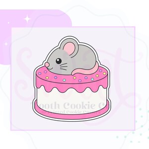 May include: A cookie cutter shaped like a gray mouse sitting on top of a round cake with pink frosting and colorful sprinkles. The cake has a white base and a pink top layer with a scalloped edge. The design features a small pink nose and tail.