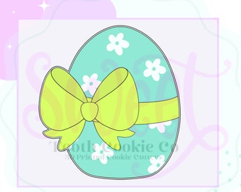 May include: A light blue Easter egg cookie cutter with a yellow bow and white flowers. The cookie cutter is designed for baking and decorating Easter cookies.