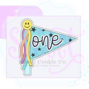 May include: A cookie cutter in the shape of a flag with the word "one" in cursive. The flag is light blue with black stars. A yellow smiley face is at the top with rainbow streamers.