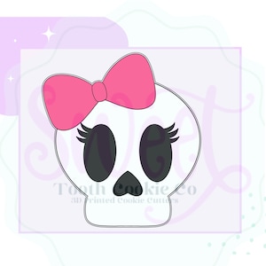 May include: A white skull cookie cutter with a pink bow, eyelashes, and black eyes.  The cutter is for making cookies in the shape of a skull.