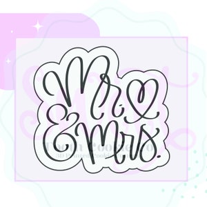 May include: A black and white cookie cutter with the words "Mr & Mrs" in a cursive font. The cutter is shaped like a heart.