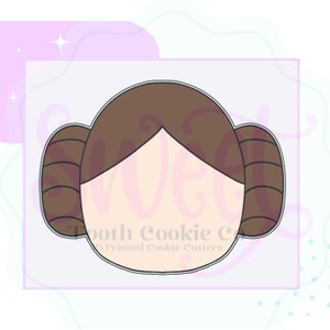 May include: A brown cookie cutter in the shape of a woman's head with a bun on each side. The cookie cutter is for making cookies.