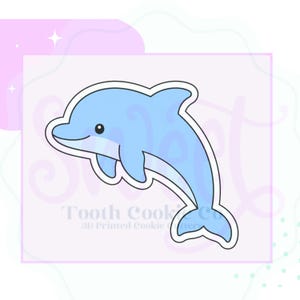 May include: A light blue dolphin-shaped cookie cutter with a white outline. The design features a smooth, curved silhouette of a jumping dolphin. The text Sweet Tooth Cookie Co 3D Printed Cookie Cutters is visible in the background.