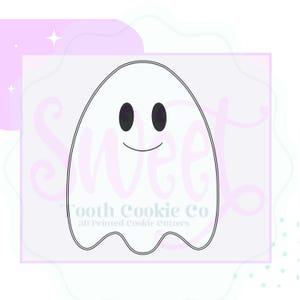 May include: A black and white ghost-shaped cookie cutter with a smiling face. The cookie cutter is outlined in black and has two oval eyes. The text "Tooth Cookie Co 3D Printed Cookie Cutters" is printed below the ghost.
