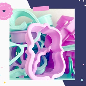 May include: A collection of pastel-colored plastic cookie cutters in various shapes, including a large, ornate, pink, curly design.