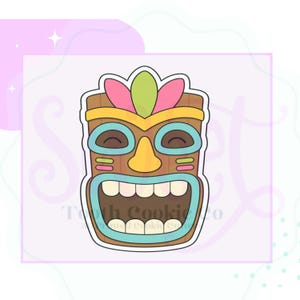 May include: A brown tiki mask cookie cutter with a yellow headband, pink and green feathers, light blue eye outlines, a yellow nose, and a wide open mouth showing white teeth. The design features a wood grain texture and a white border outline.