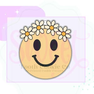 May include: A yellow smiley face with a daisy flower crown. The smiley face has black eyes and a curved black mouth. The text "Tooth Cookie Co. Printed Cookie Cutters" is visible.
