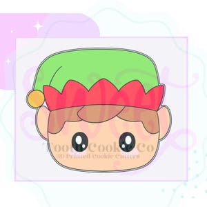 May include: A 3D-printed cookie cutter in the shape of an elf's face. The elf has a green hat, red trim, and a yellow ball on the side. The text "Toot Cook Co" and "3D Printed Cookie Cutters" are printed on the face.