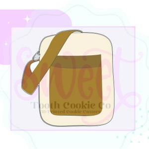 May include: A beige and brown crossbody bag with a zipper closure and a brown strap. The bag has a large pocket on the front. The text "Tooth Cookie Co. 3D Printed Cookie Cutters" is printed on the bag.