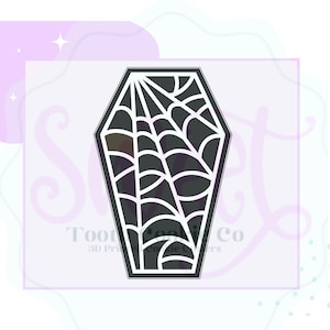 May include: Black and white 3D printed cookie cutter shaped like a coffin with a spider web design.