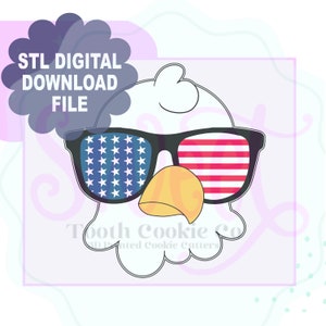 May include: A white eagle cookie cutter with a black outline, wearing sunglasses with an American flag design. The sunglasses have a red, white, and blue pattern. The text "Tooth Cookie Co. 3D Printed Cookie Cutters" is below the eagle.