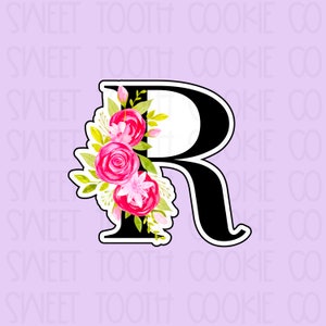 May include: A black letter R with a floral design. The flowers are pink, white, and green. The letter is outlined in black.