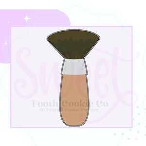 May include: A brown makeup brush cookie cutter with a white handle. The brush is shaped like a fan and has a textured design.