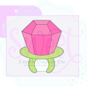 May include: A pink and green cookie cutter shaped like a ring with a large diamond on top. The cookie cutter is for making cookies in the shape of a ring with a diamond.