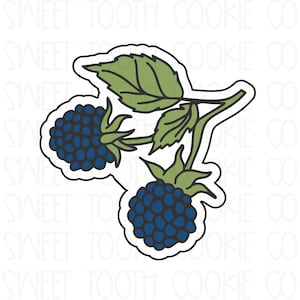 May include: A cookie cutter in the shape of a blackberry branch. The design features two dark blue blackberries with green stems and leaves. The outline is black with a white border.