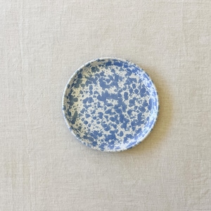May include: A round plate featuring a speckled pattern with blue paint splatters on a white background. The plate has a smooth, circular rim and a flat surface, displaying a consistent mottled design across the entire top face of the dish.