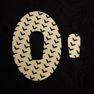 May include: A white and black patterned circle with a black circle cut out of the centre, forming the shape of the number zero. The pattern is made up of small black chevrons on a white background.