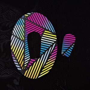 May include: A colorful, striped, oval-shaped sticker with a hole in the center. The sticker has a rainbow pattern with black stripes. There is a smaller, rectangular sticker with a similar pattern.