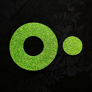 Könnte beinhalten: Zwei grüne Glitzerkreise, einer größer als der andere, mit einem Loch in der Mitte des größeren Kreises.