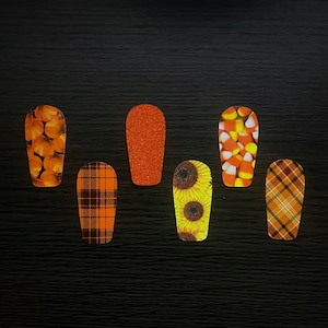 May include: Six different nail art designs featuring fall themes. The designs include pumpkins, plaid, sunflowers, and candy corn.