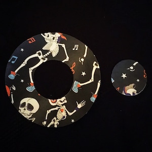 May include: Two round stickers with a black background and a white skeleton design. The larger sticker has a hole in the centre. Both stickers feature musical notes and stars.