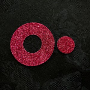 May include: Two pink glitter circles, one larger than the other, with a hole in the centre of the larger circle.