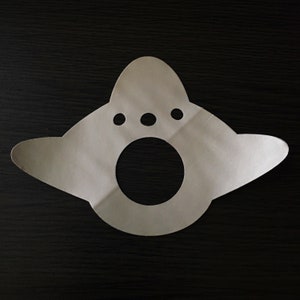 May include: A white paper cutout of a UFO with three small circles and a large circle in the center.