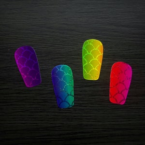 May include: Four nail art designs with a mermaid scale pattern. Each nail has a different color gradient: purple, blue-green, yellow-green, and red-pink. The scales have a glittery effect.